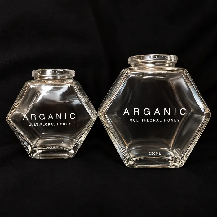 Two hexagonal glass honey jars printed in white with the Arganic label